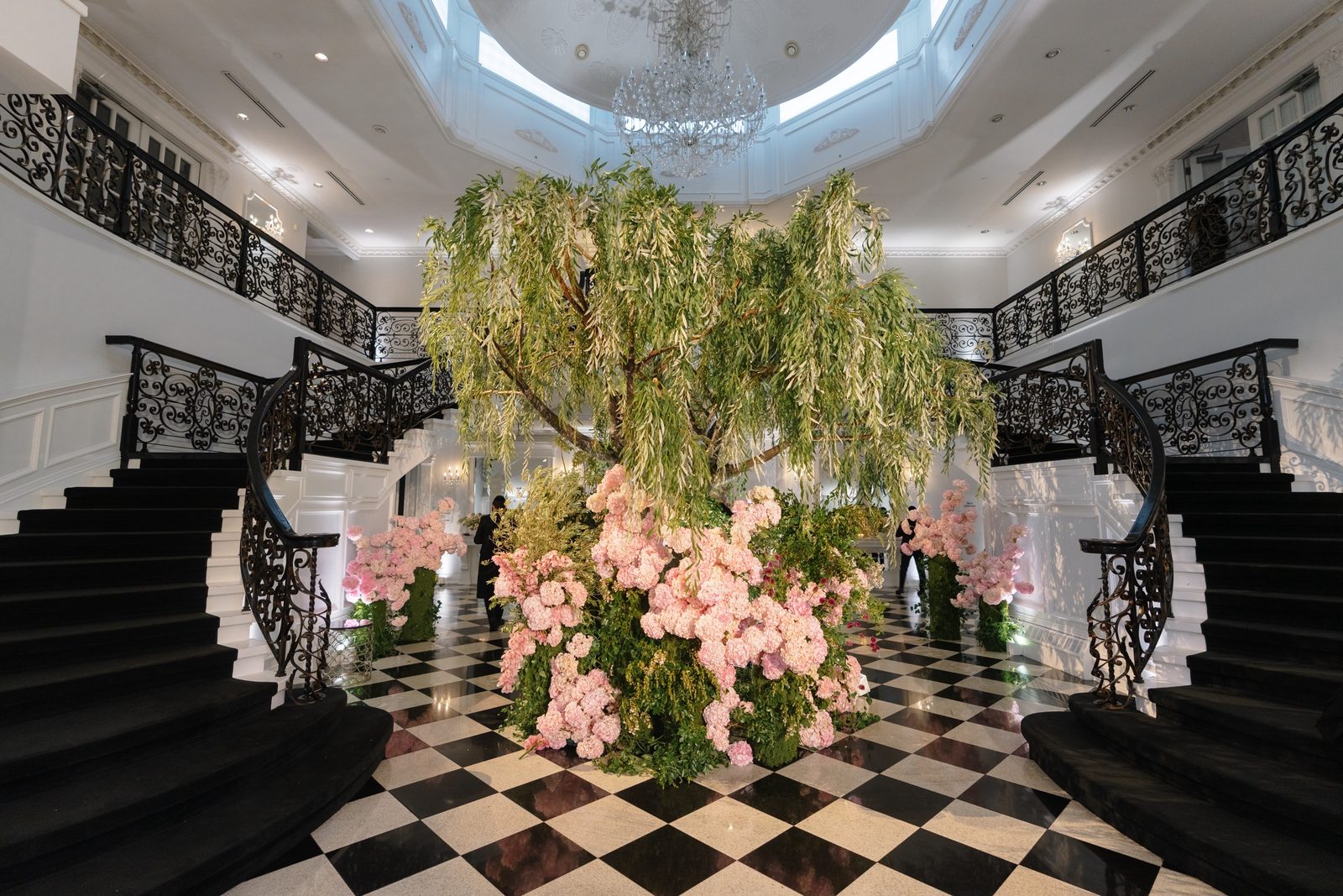 The foyer at The Addison Park with a weeping willow installation, pink hydrangeas and the double staircase