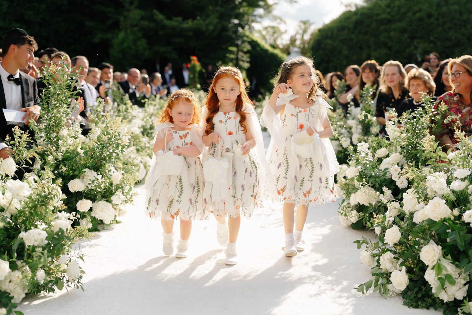 Flower girls walking down the aisle between white florals