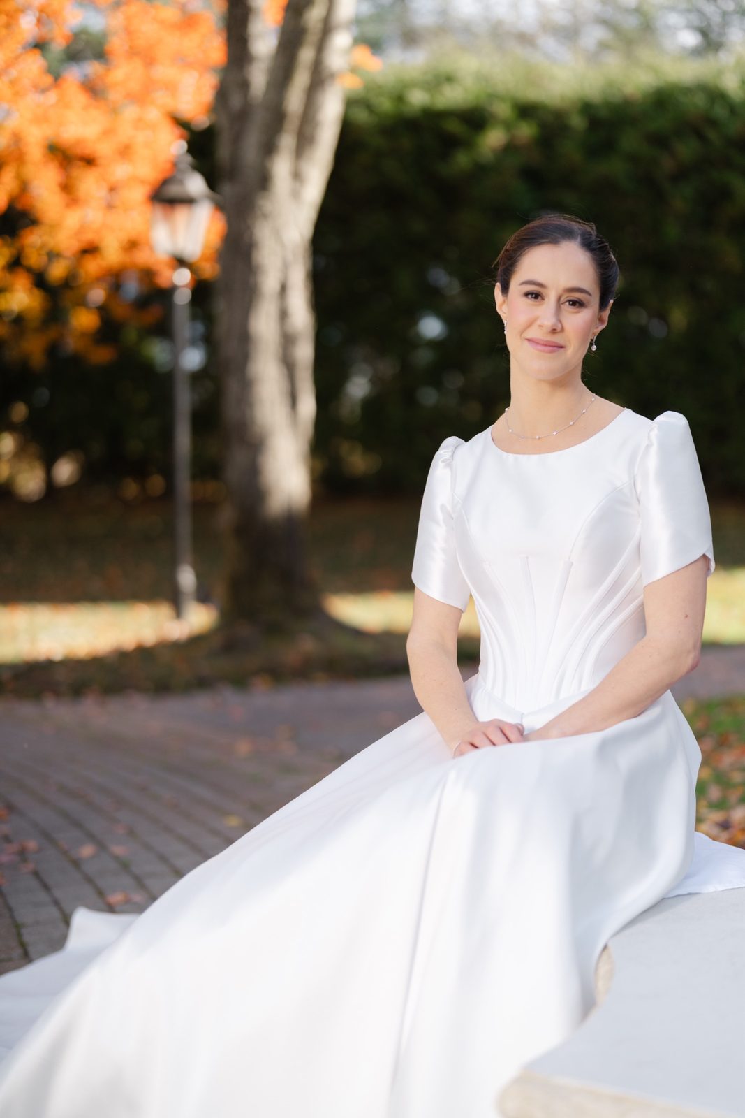 Kayla seated on a stone bench among fall leaves