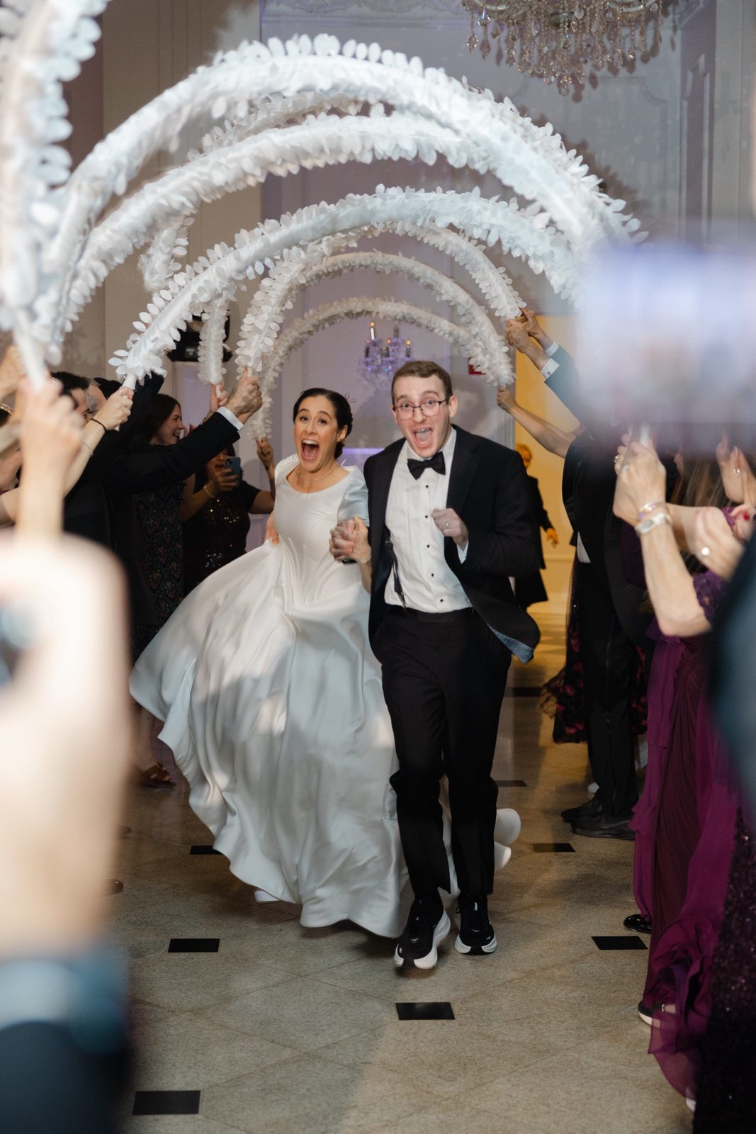 Kayla and Gabriel entering the ballroom under feather arches