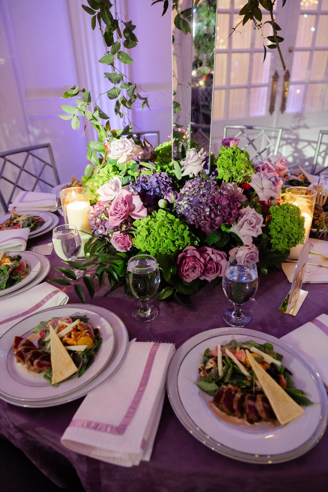 A purple and green centerpiece on a plum tablecloth