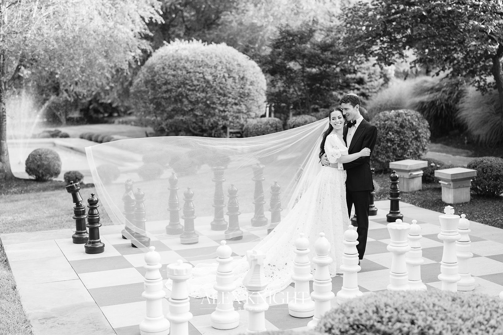 Aline and Tyler on the oversized outdoor chess board, her veil stretched across it