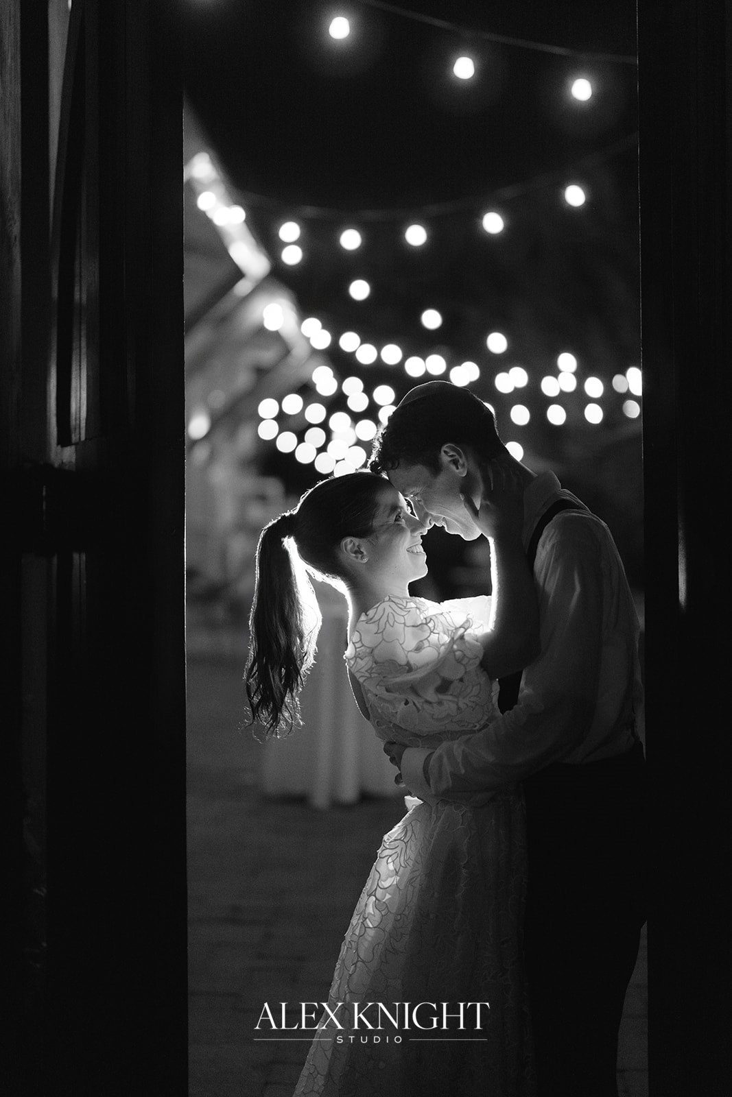 Aline and Tyler under the string lights at night, in black and white