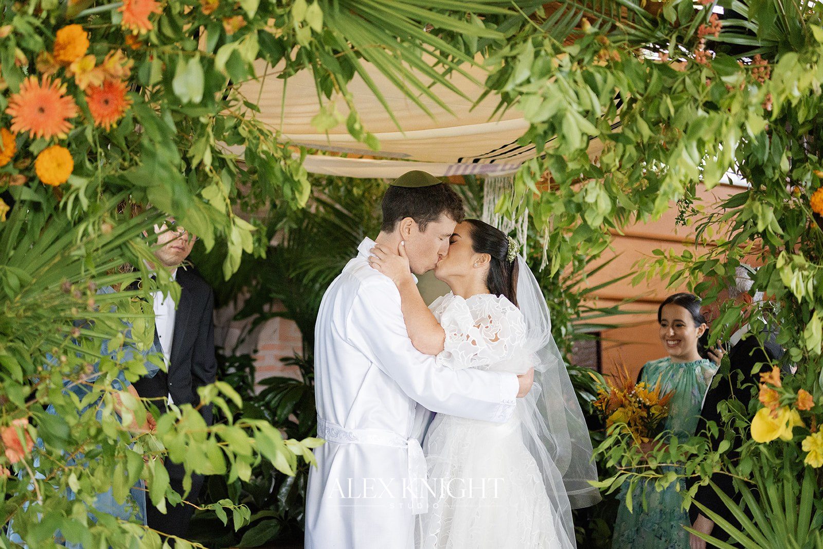 Aline and Tyler’s first kiss under the greenery chuppah