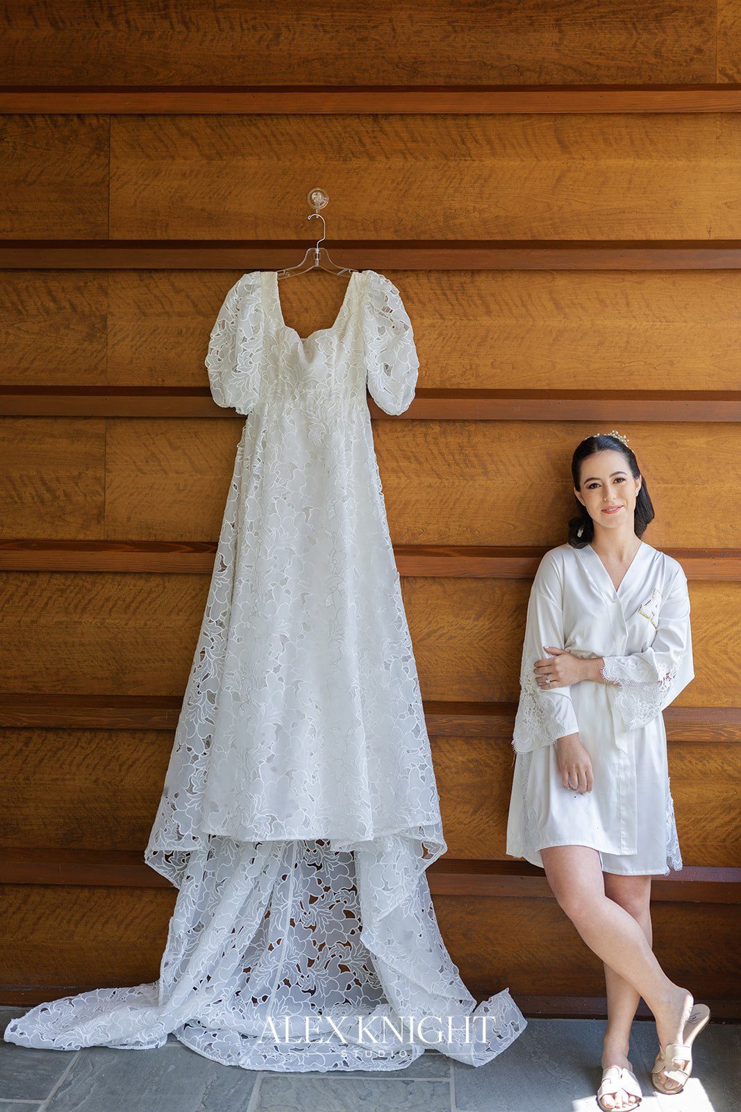 Aline in her robe beside her gown, hung on a wood-paneled wall