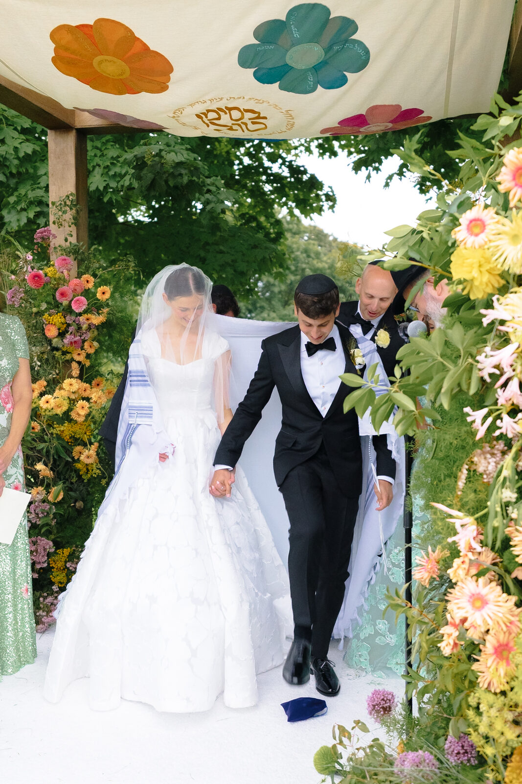 Charlie walks to the chuppah beneath a hand-painted floral canopy