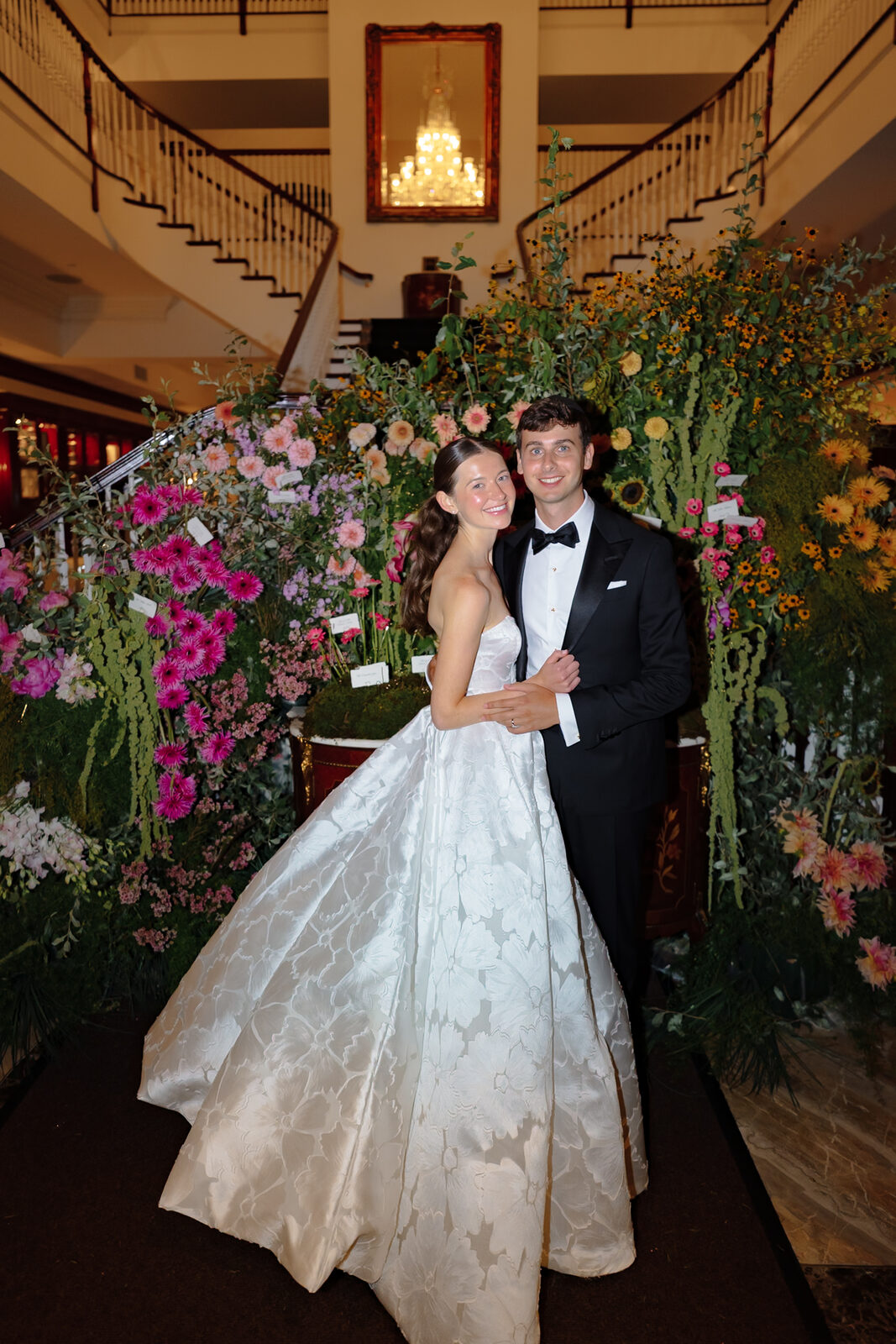 Allie and Charlie on the staircase framed by tall wildflower arrangements