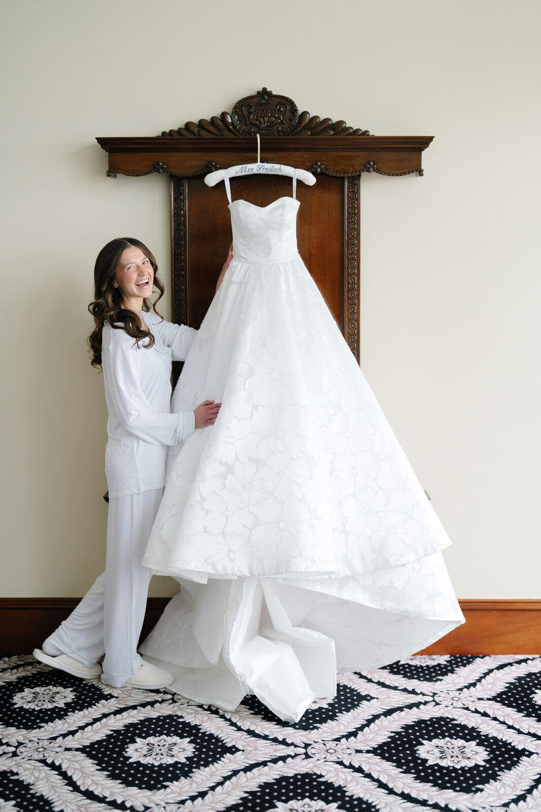 Allie in white pajamas beside her gown hanging in the suite at Trump National Westchester