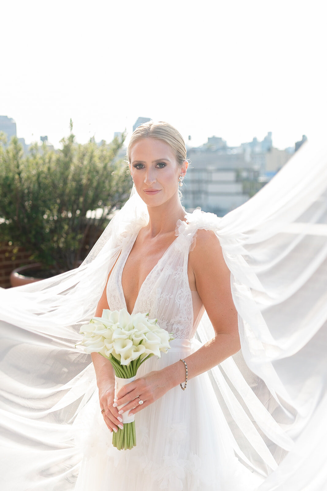 Ashley holds a bouquet of white calla lilies as her veil catches the wind