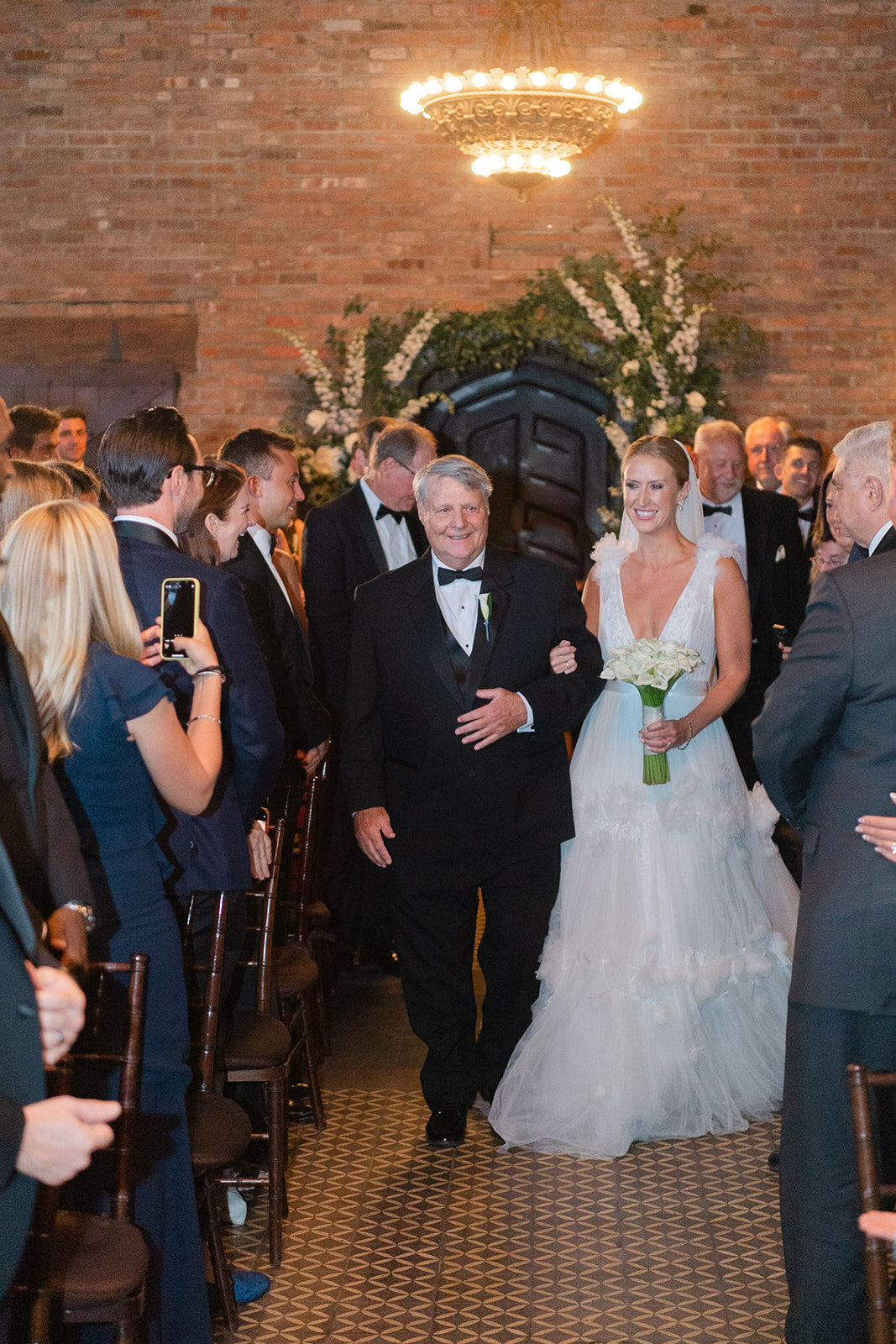 Ashley walks down the aisle with her father under the chandeliers