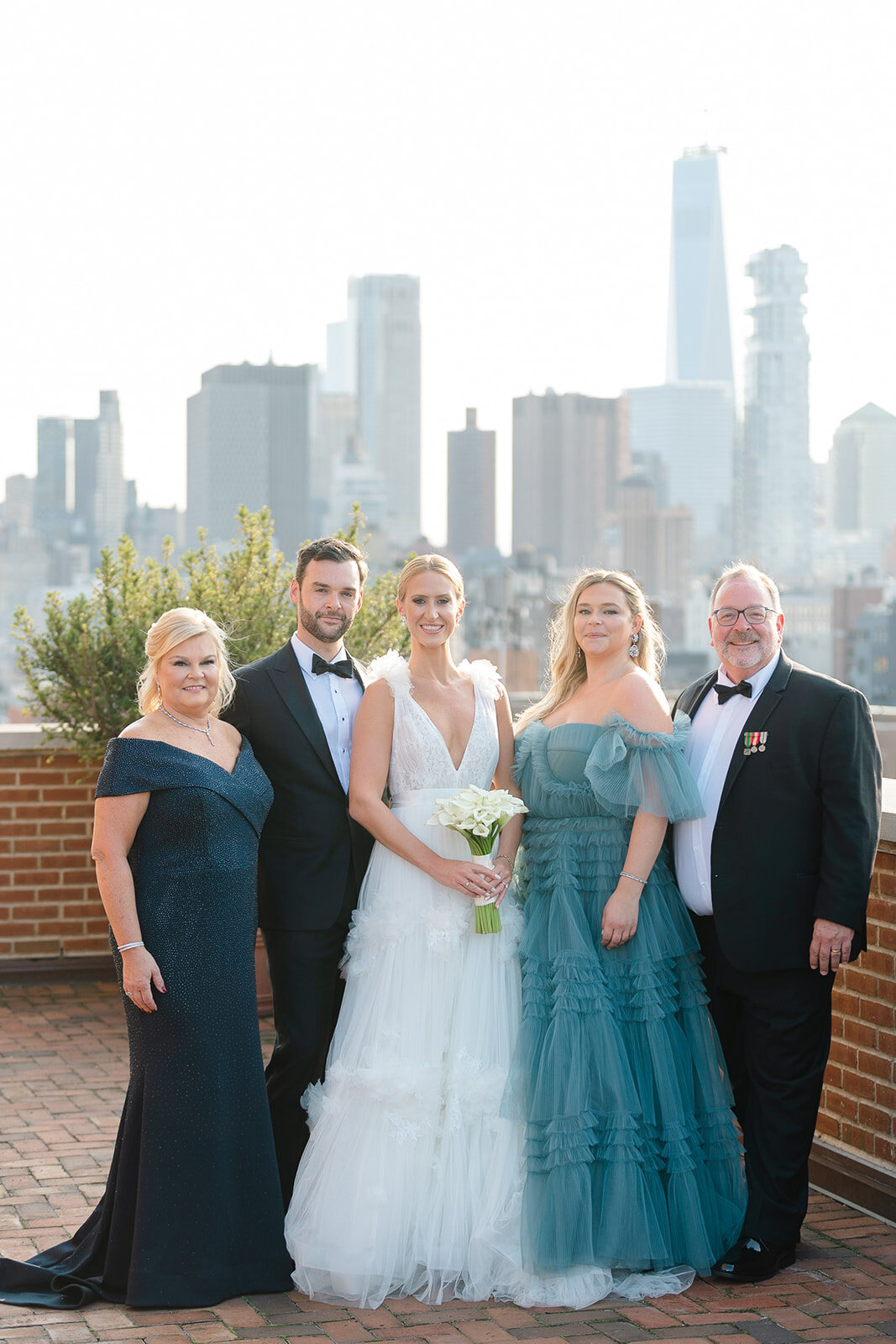 Ashley and Kendall with their families on the rooftop terrace, the skyline behind them