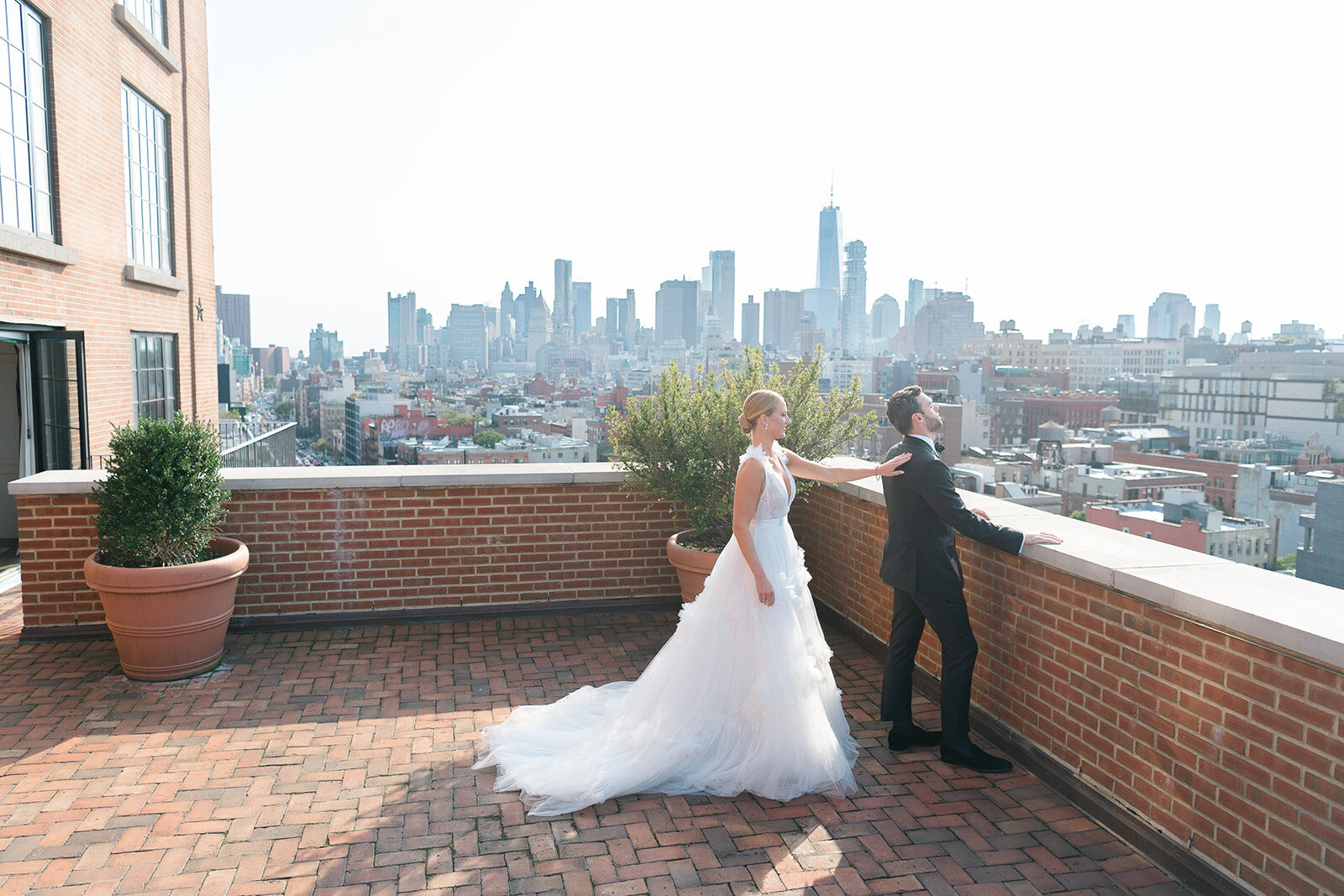 Ashley walks across the brick terrace toward Kendall for their first look, the Manhattan skyline behind them