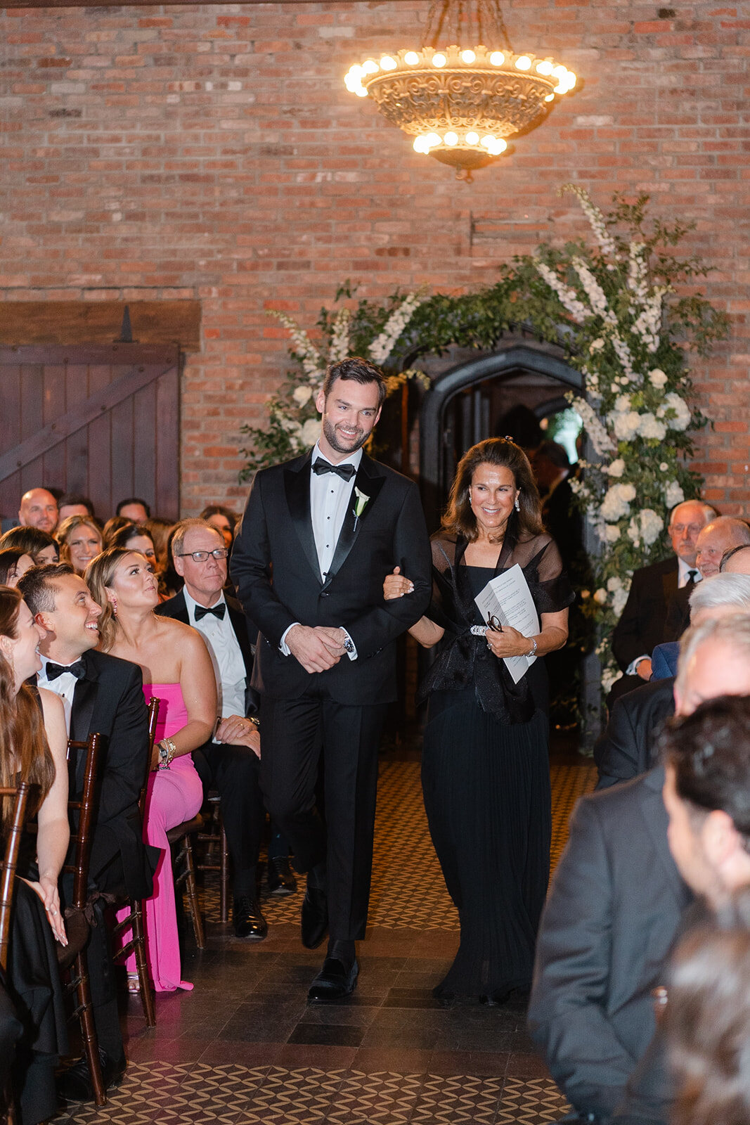 The processional into the brick ceremony room with the fireplace altar and white florals