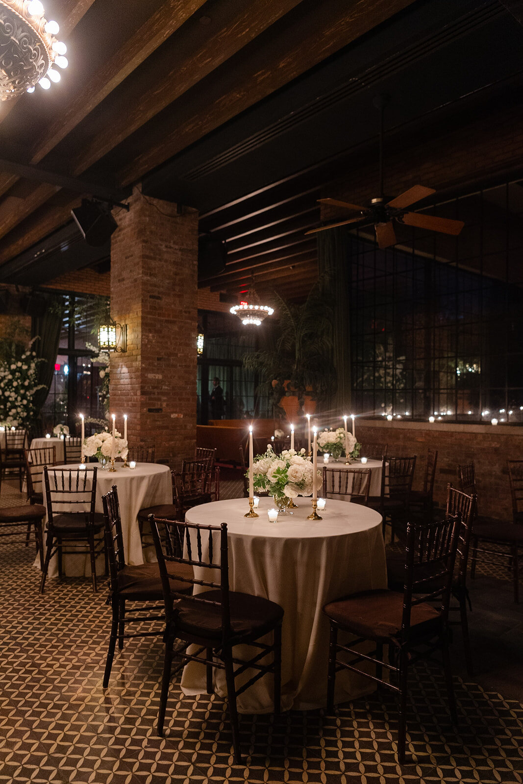 Reception tables with ivory linens, white roses and candles under the Bowery’s wooden beams