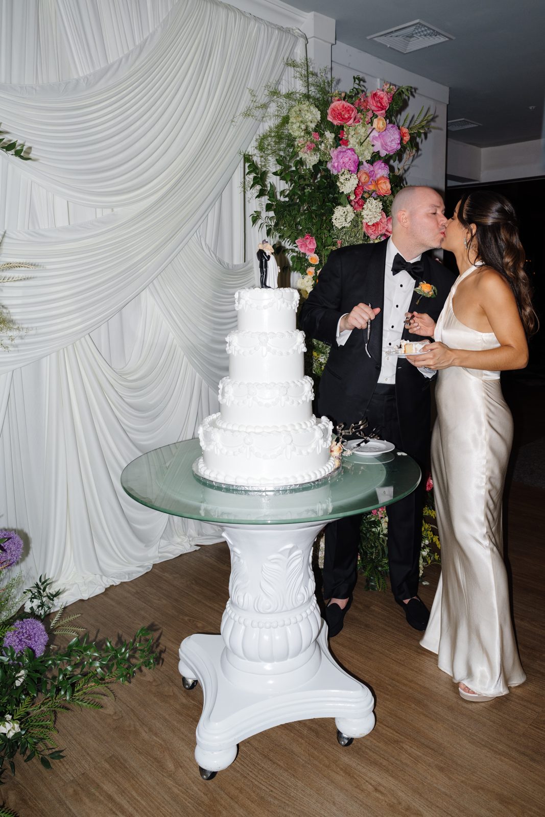 Cutting the cake beside the draped wall of florals
