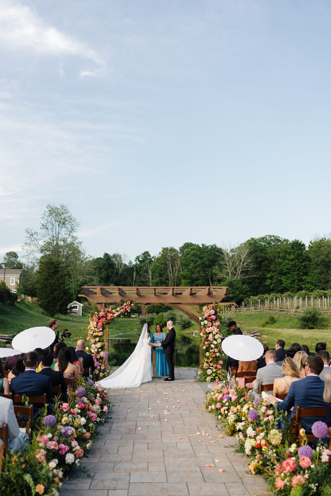 The outdoor ceremony at Bear Brook Valley under a pergola of pink and coral florals