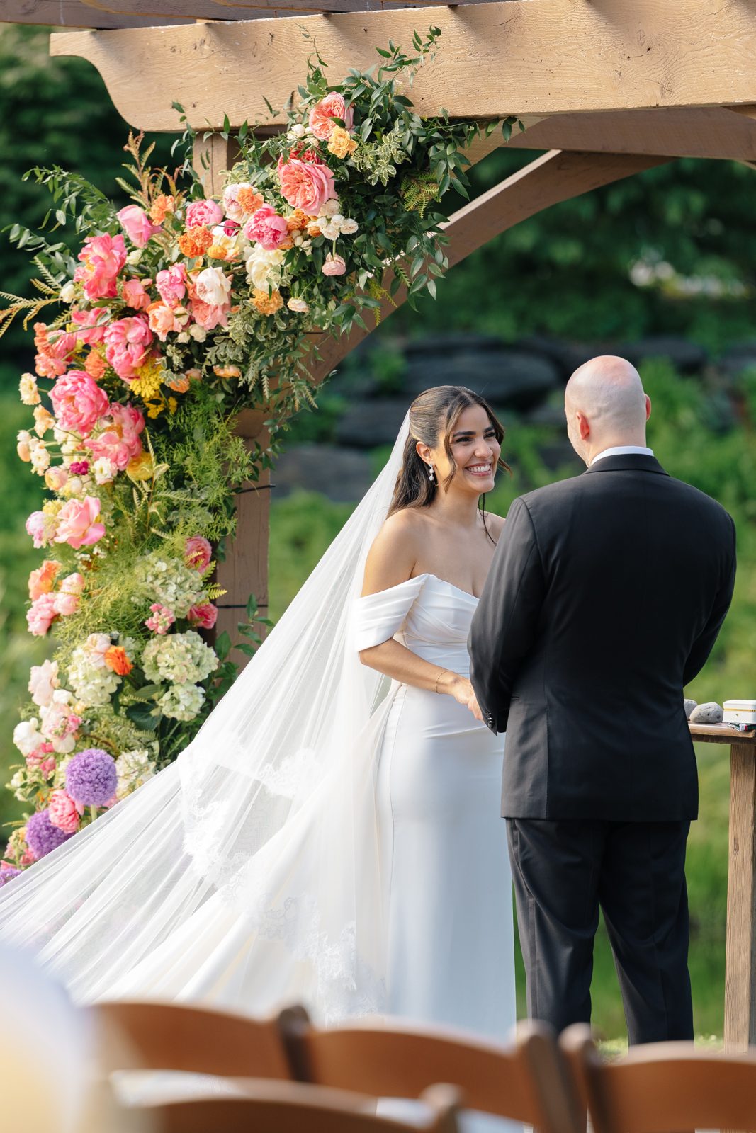 The outdoor ceremony at Bear Brook Valley under a pergola of pink and coral florals