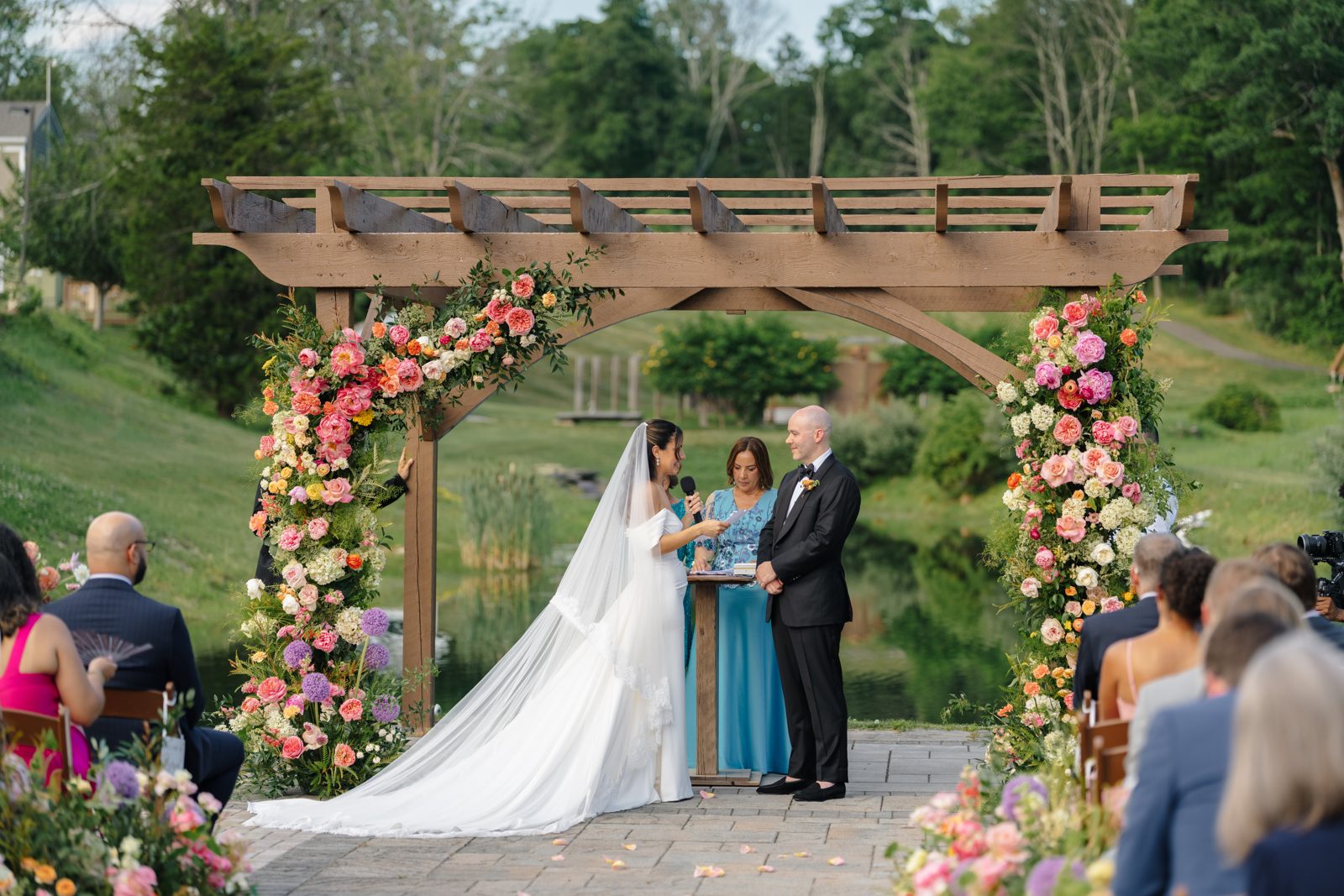 The outdoor ceremony at Bear Brook Valley under a pergola of pink and coral florals