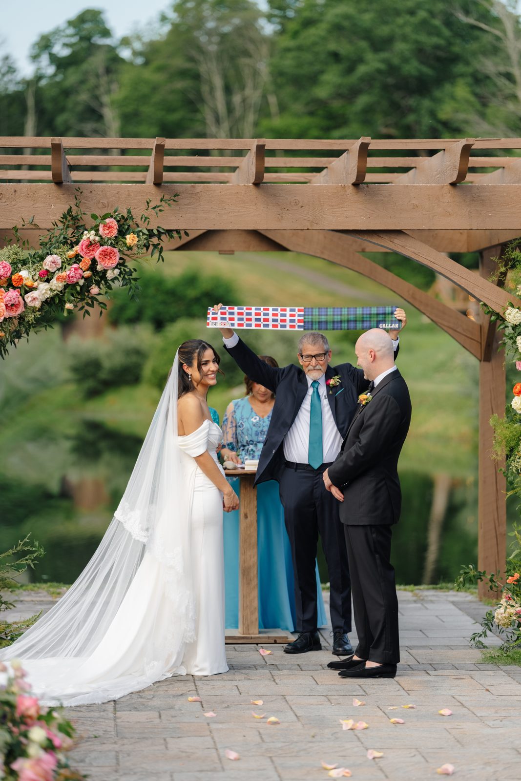 The outdoor ceremony at Bear Brook Valley under a pergola of pink and coral florals