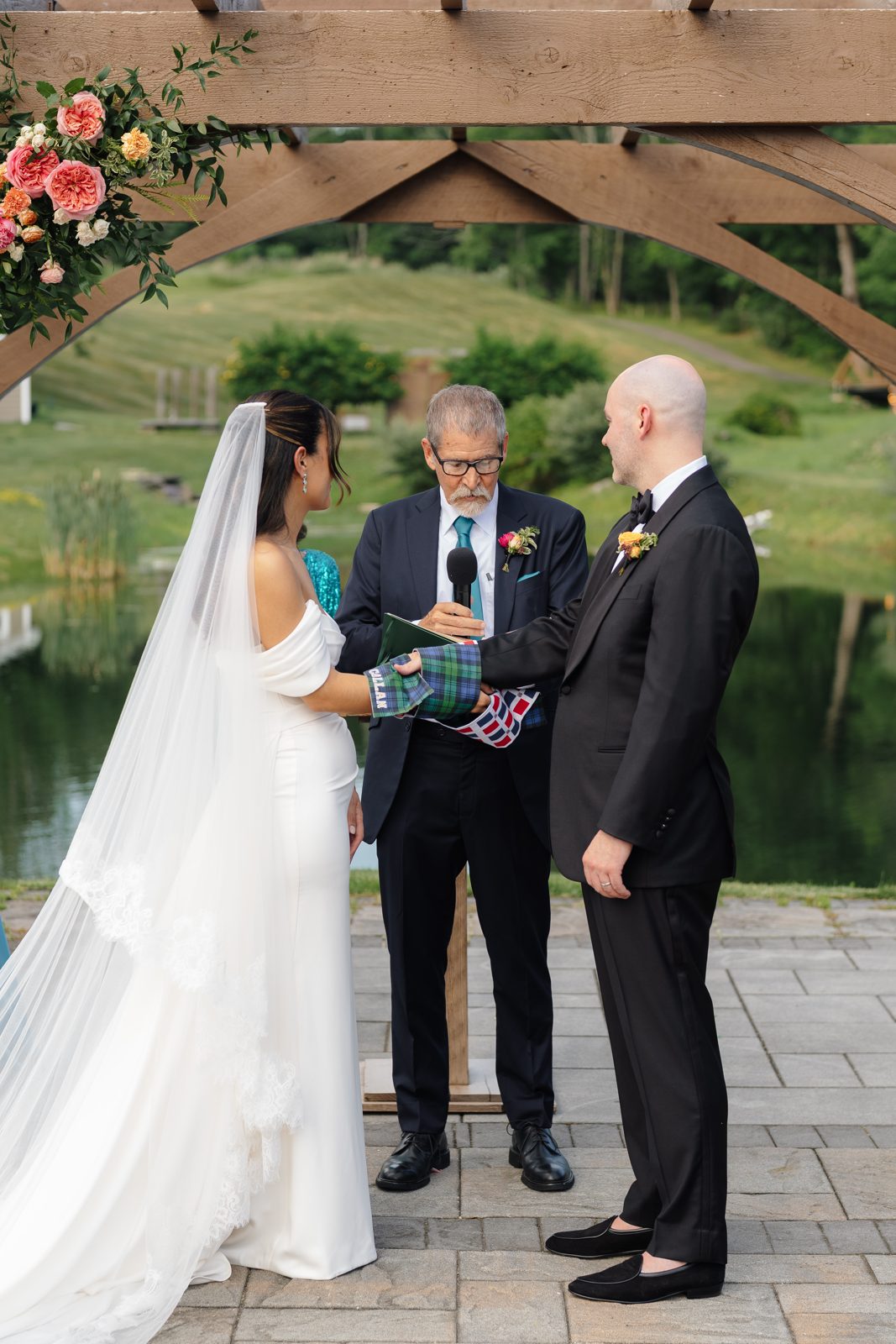 The outdoor ceremony at Bear Brook Valley under a pergola of pink and coral florals