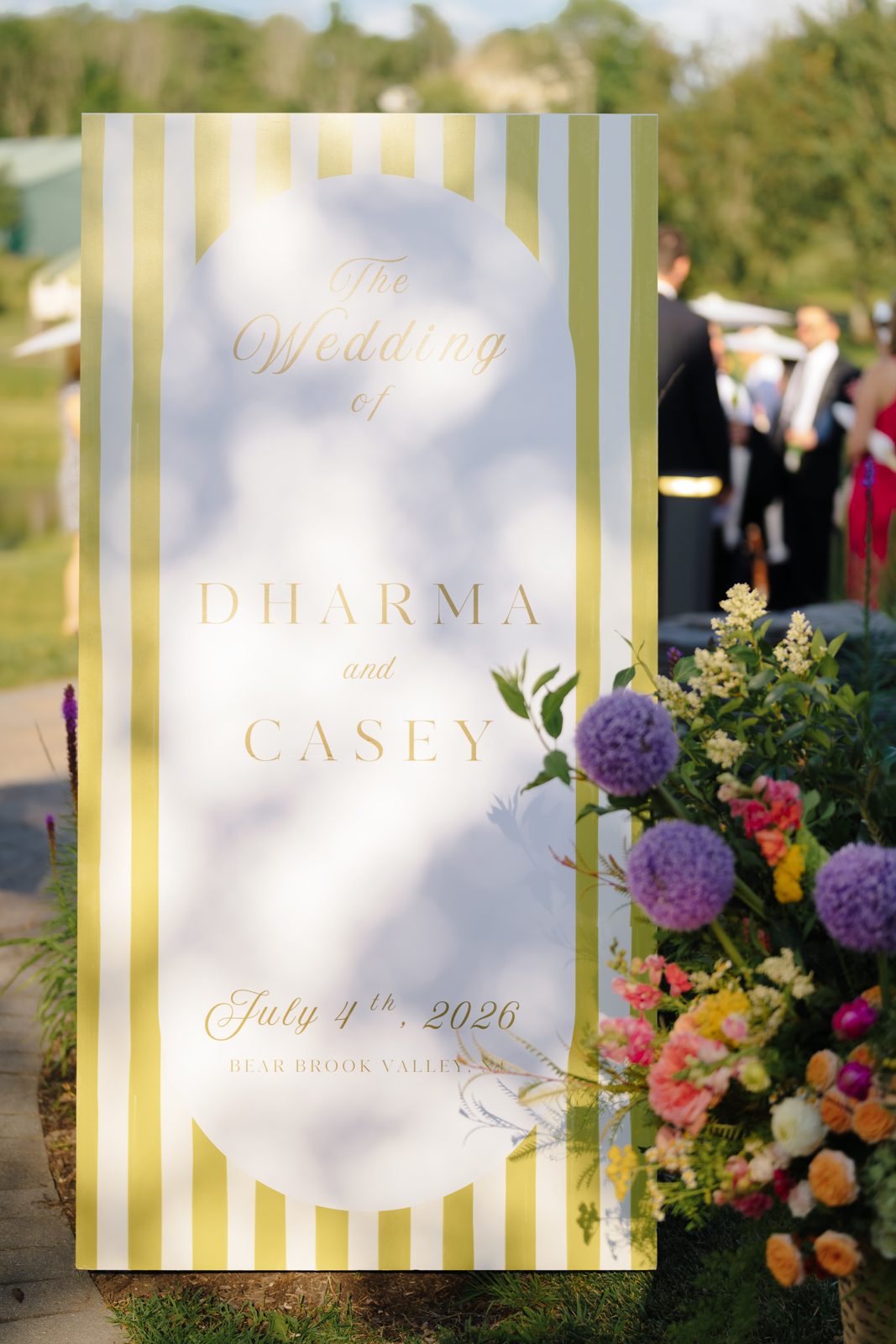 The striped Dharma and Casey welcome sign wrapped in summer florals at Bear Brook Valley