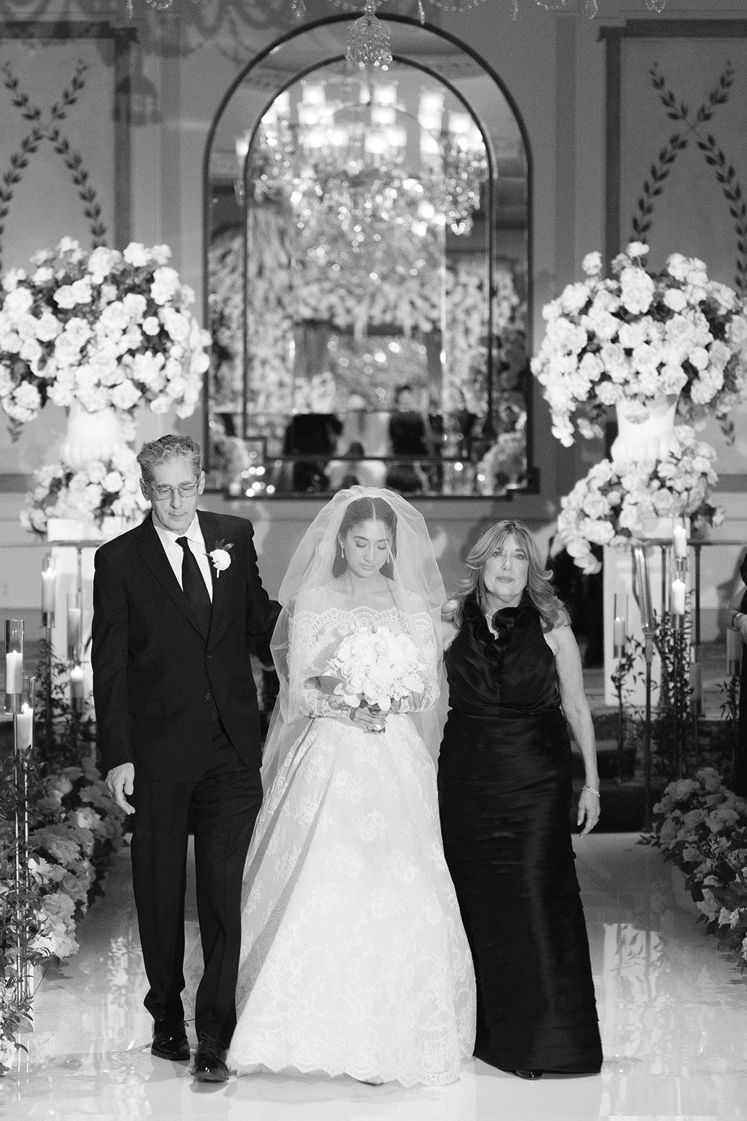 Dori walking down the aisle with her parents, black and white