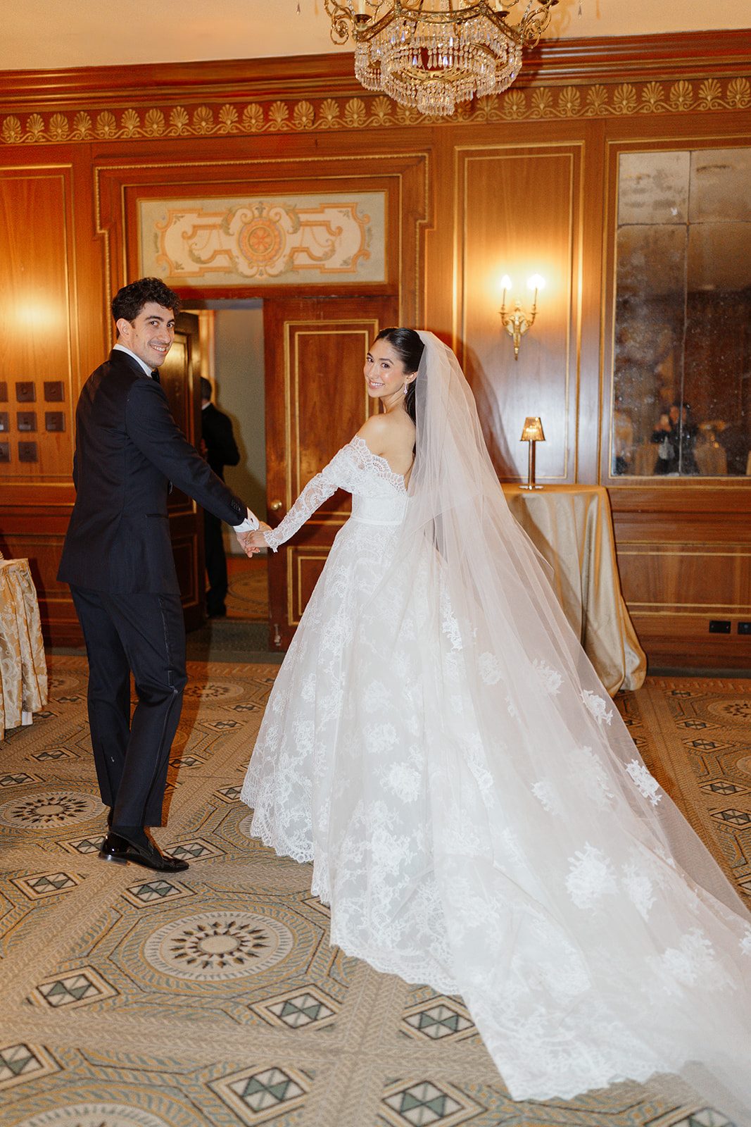 Dori and Ben hand in hand in a wood-paneled room at The Pierre