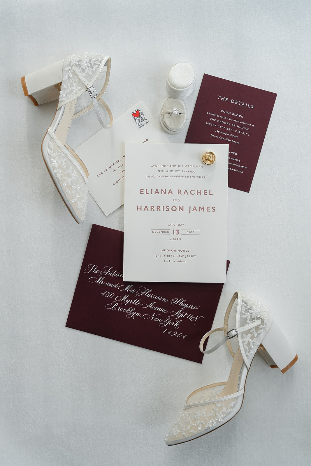 The invitation suite in burgundy and white beside Ellie’s bridal heels