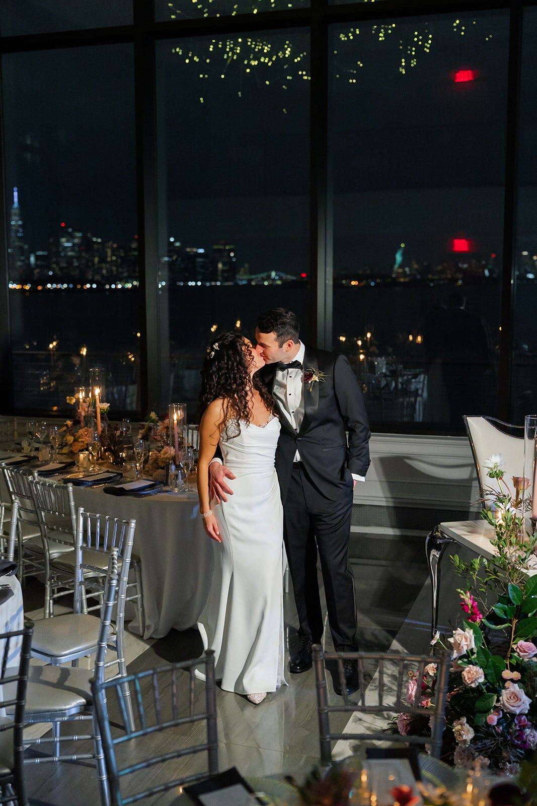 Ellie and Harrison at the ballroom windows with the city lit up at night