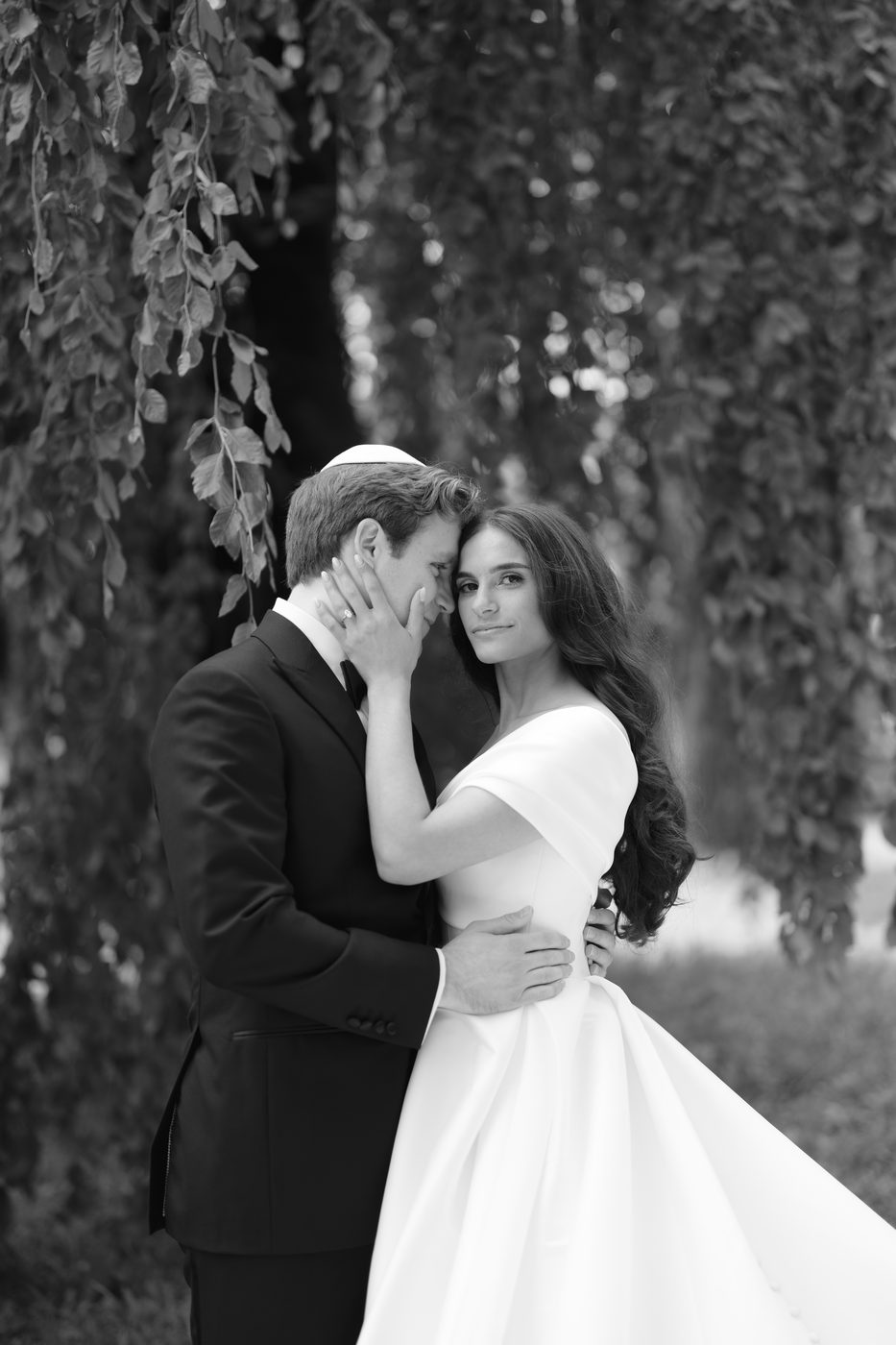 Black and white portrait of the couple beneath a weeping willow, her hand resting on his cheek.