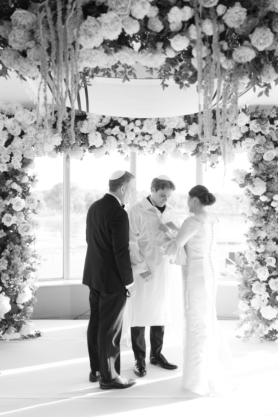 Black and white photo of the ring being placed beneath the chuppah, the groom in his kittel.