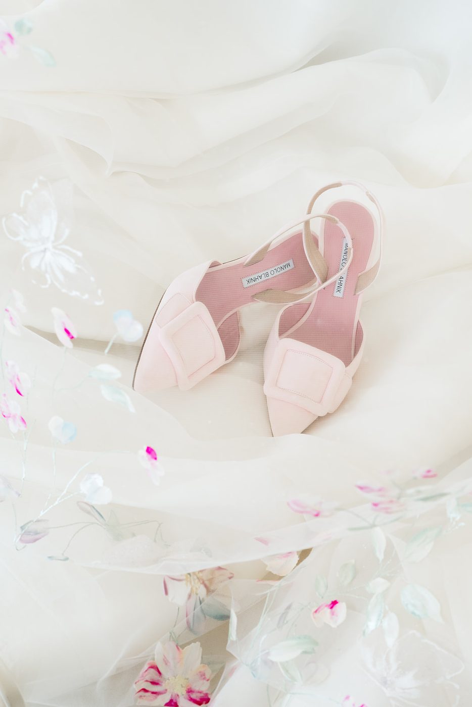 Pale pink bridal shoes resting on the embroidered gown before the bride dresses.
