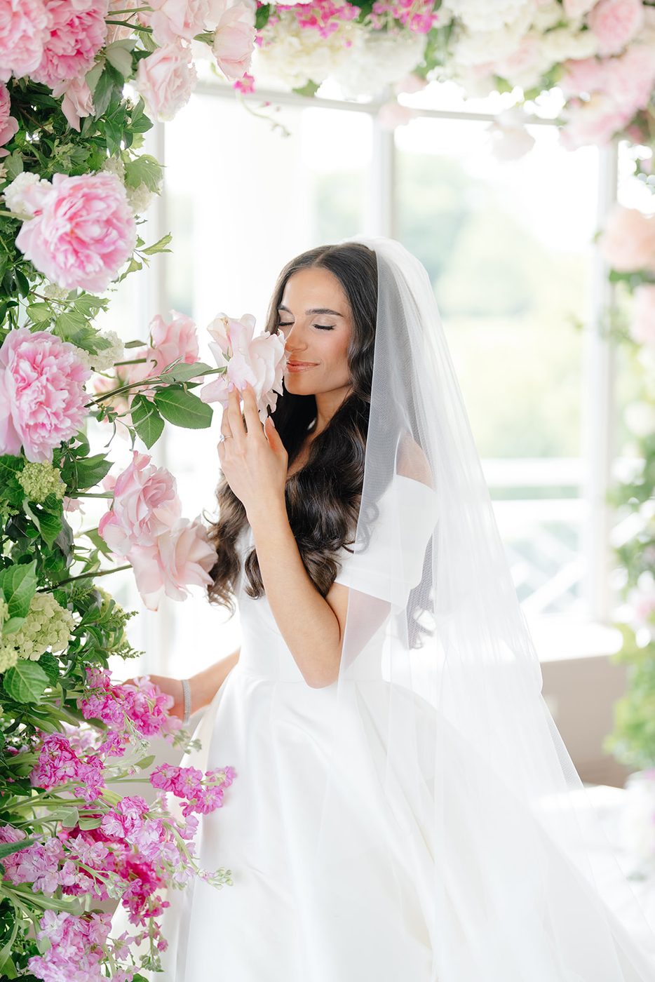 The bride beneath the floral arch, her veil catching the light from the windows.