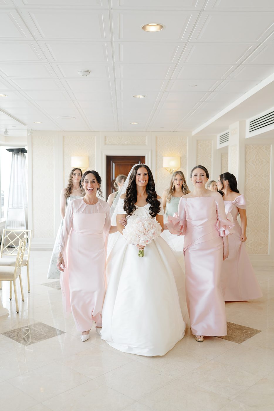The bride walks the club hallway surrounded by her bridesmaids in blush gowns.