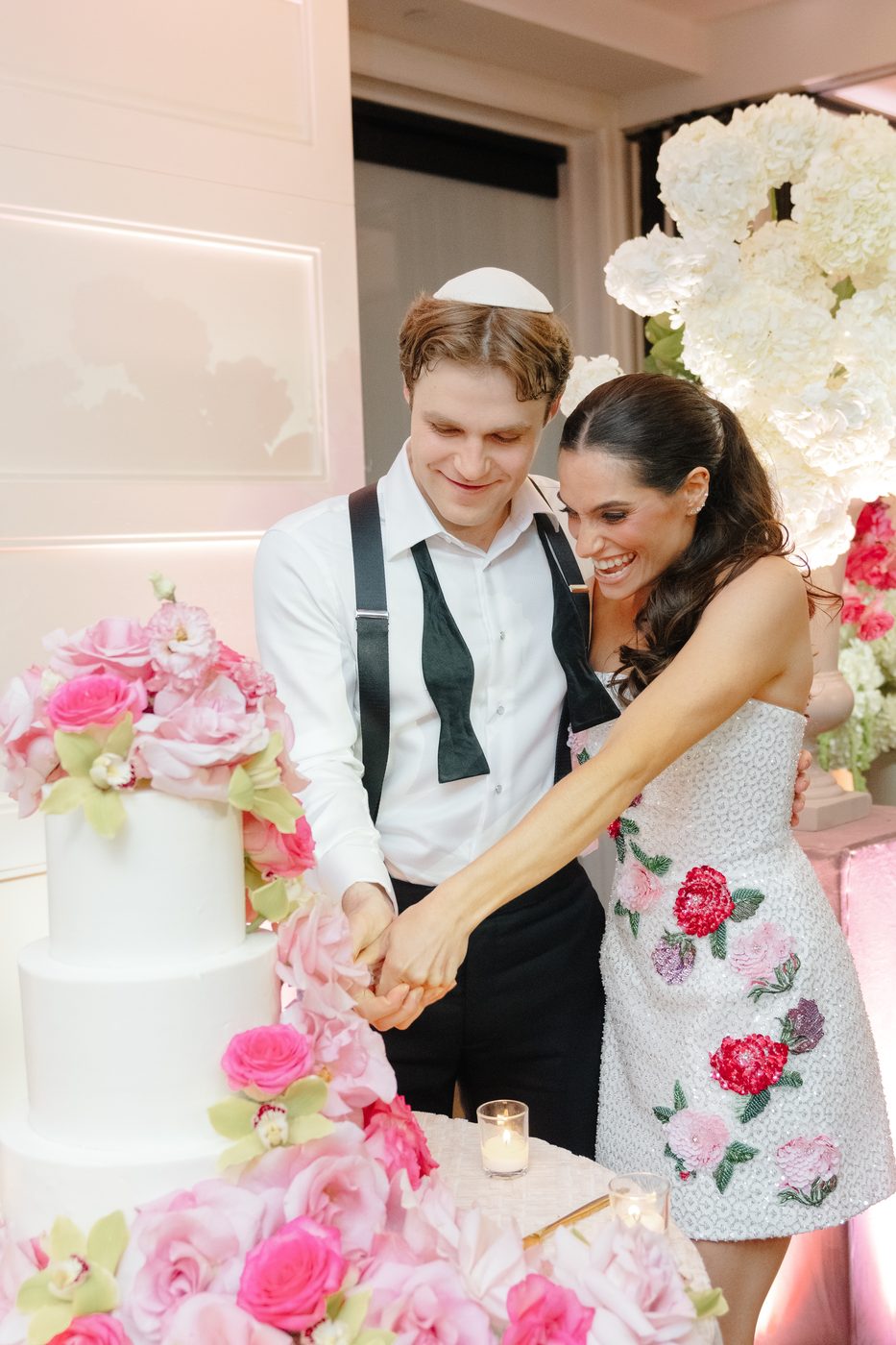 The couple cut a white tiered cake trimmed with pink garden roses and peonies, the bride now in a short embroidered floral dress.