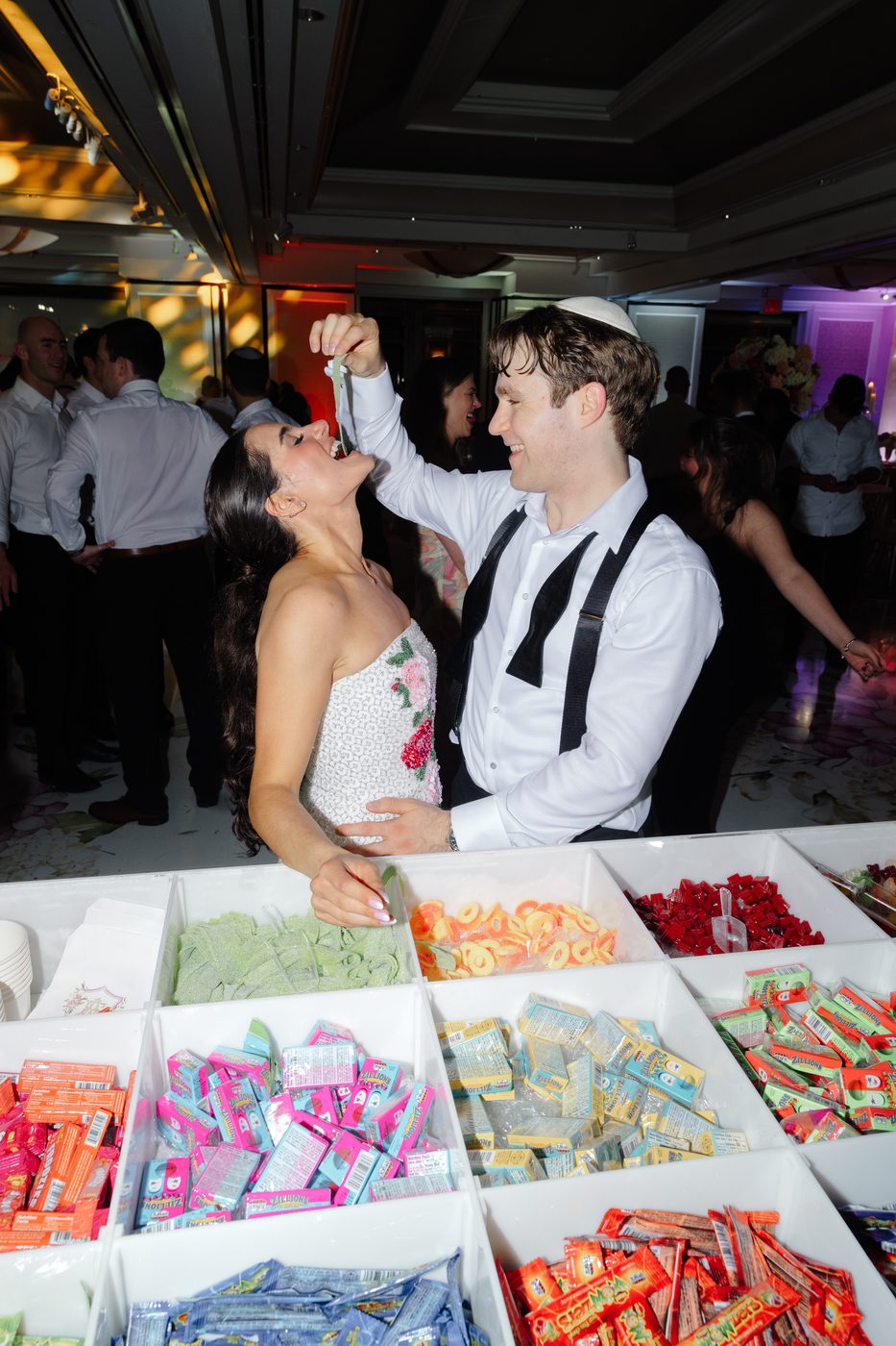 The groom feeds the bride a candy at the late-night sweets station on the dance floor.
