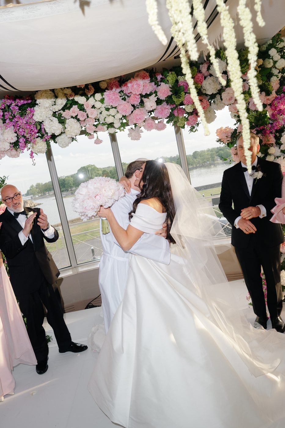 The bride and groom embrace under the chuppah as guests applaud around them.