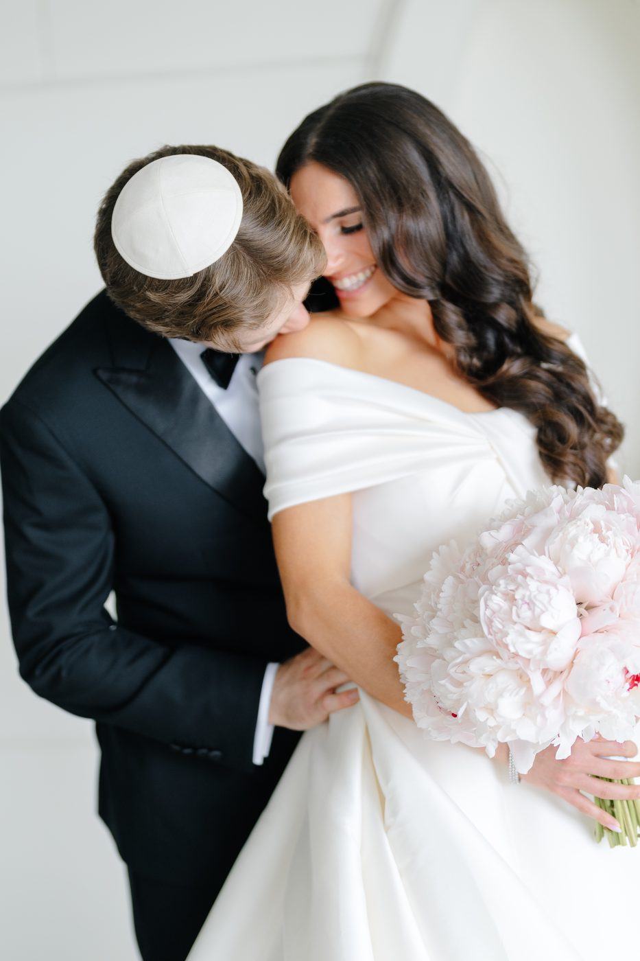 The groom holds the bride close during their first look, her blush peony bouquet at her side.
