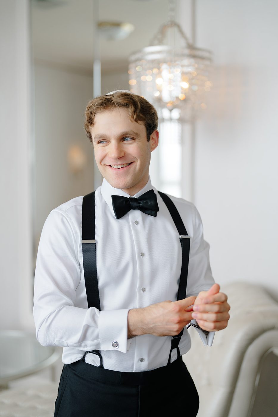 The groom fastens his bow tie and suspenders while getting ready in the Rose Suite upstairs.