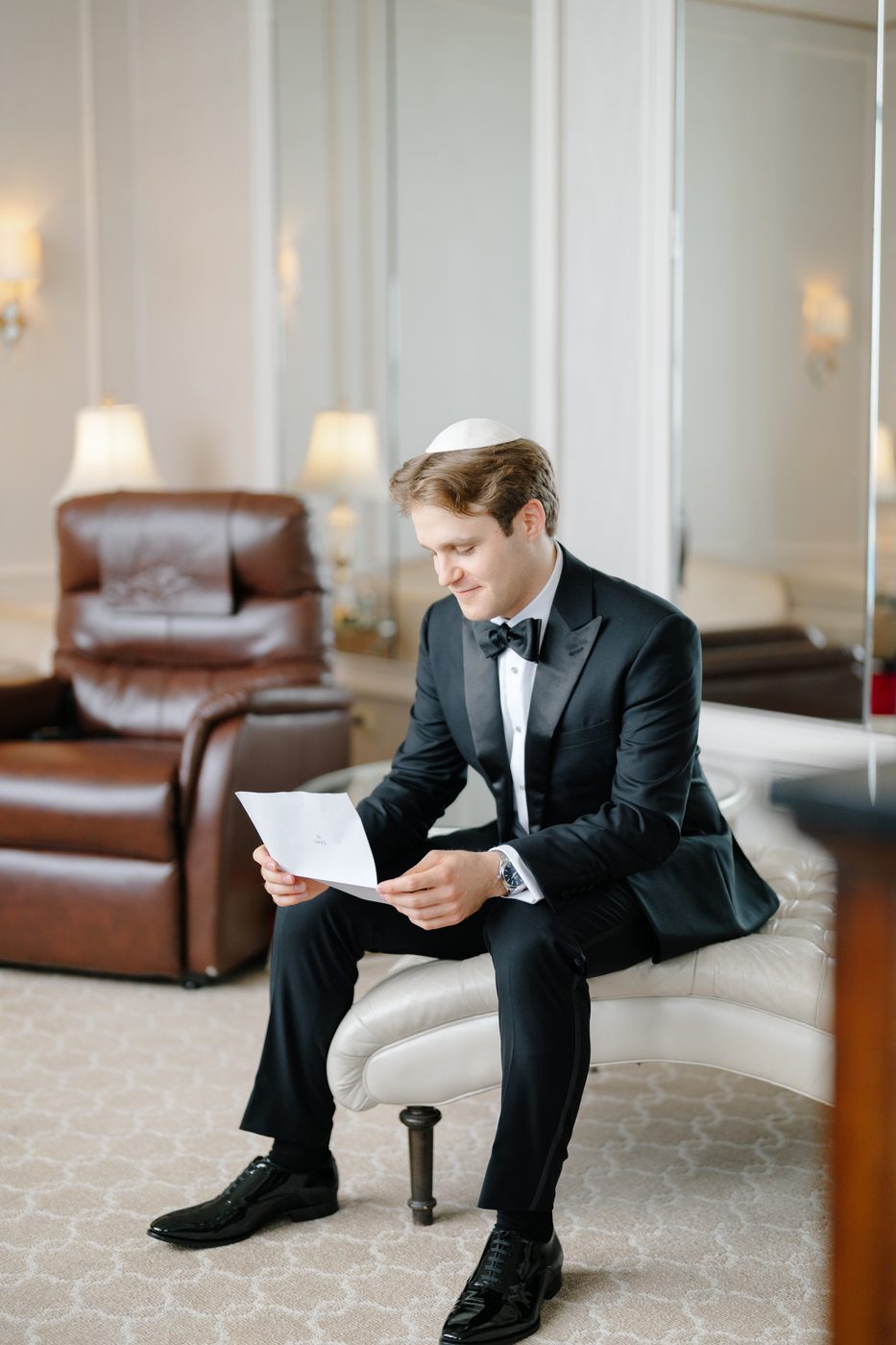The groom in a black tuxedo and kippah reads a letter from the bride in the Rose Suite before the first look.