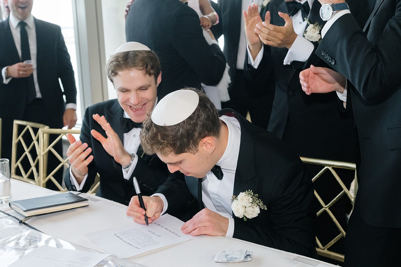 The groom signs the ketubah surrounded by family and friends at the tisch.