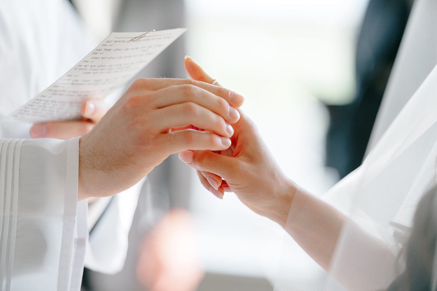 Close-up of the ring being placed on the bride's finger beneath the chuppah.