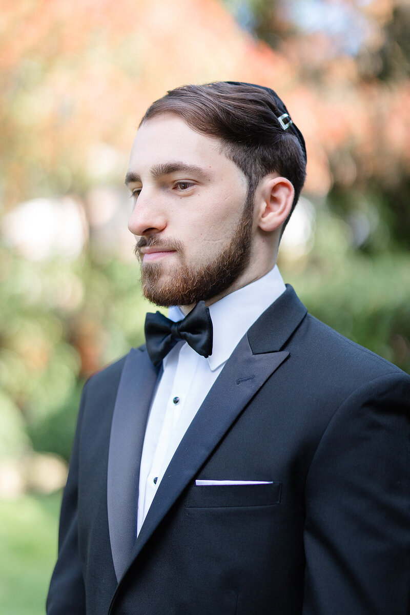 Portrait of the groom in a black tuxedo and bow tie in the gardens before the ceremony.