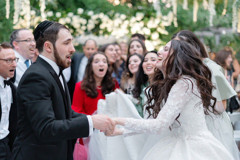 The bride and groom hold hands laughing as guests dance around them in the garden right after the ceremony.