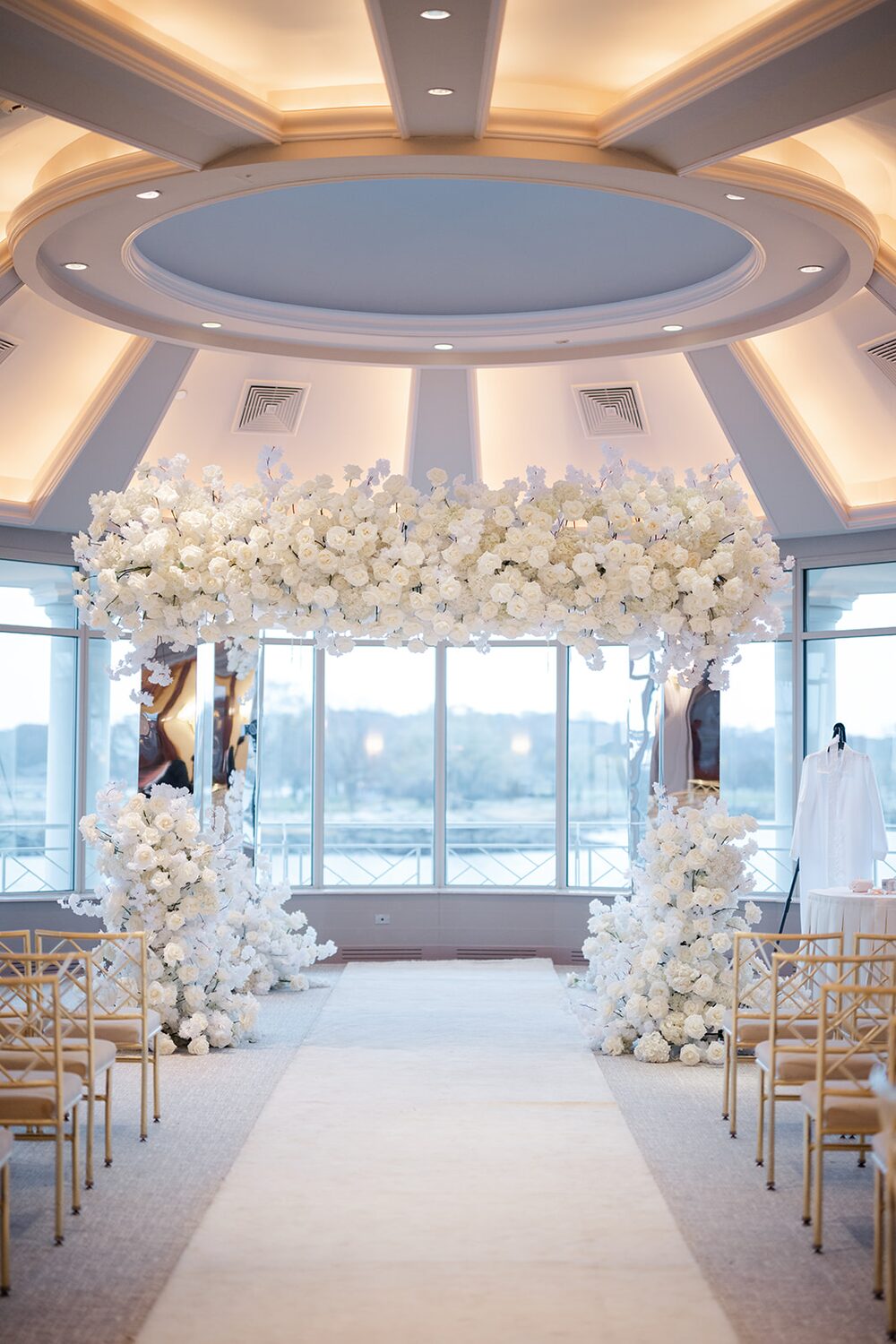 An all-white floral chuppah fills the domed ballroom, Long Island Sound visible through the glass.