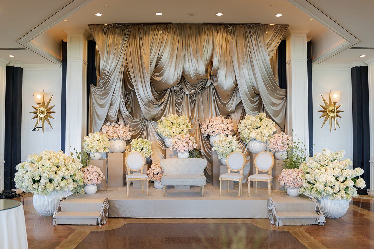The badeken stage set in gold drapery, loveseat flanked by blush and cream florals.