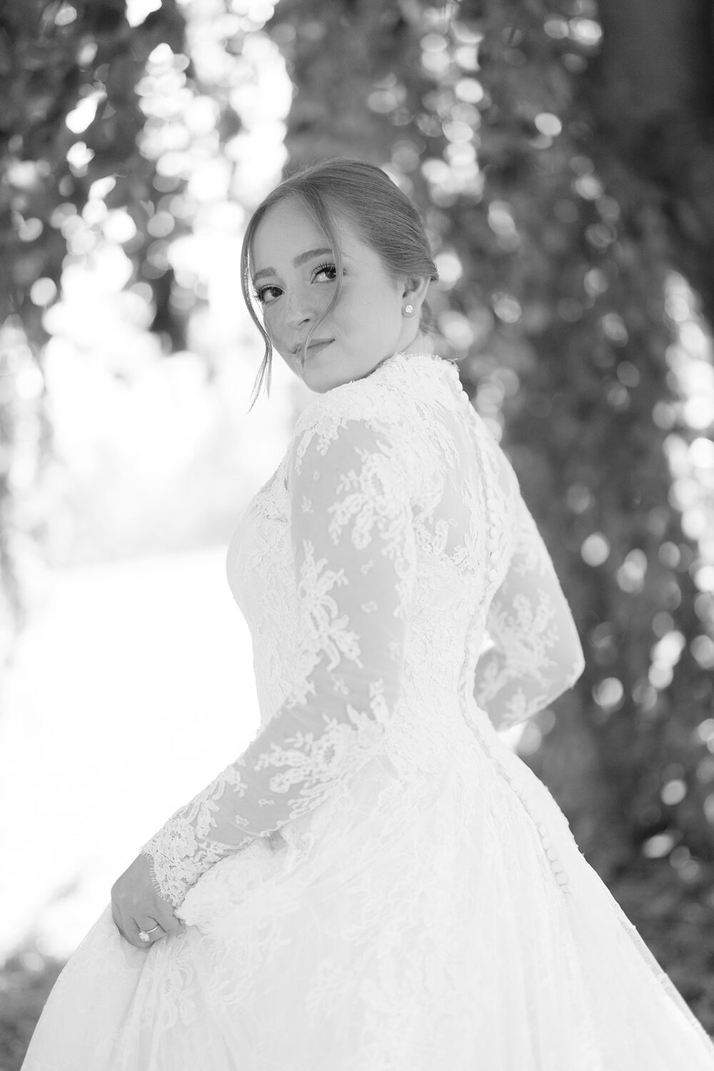 A black and white portrait of the bride in long lace sleeves beneath the leaves.