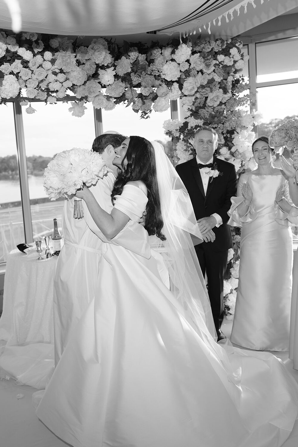 A black and white moment under the chuppah as the couple stands with their parents.