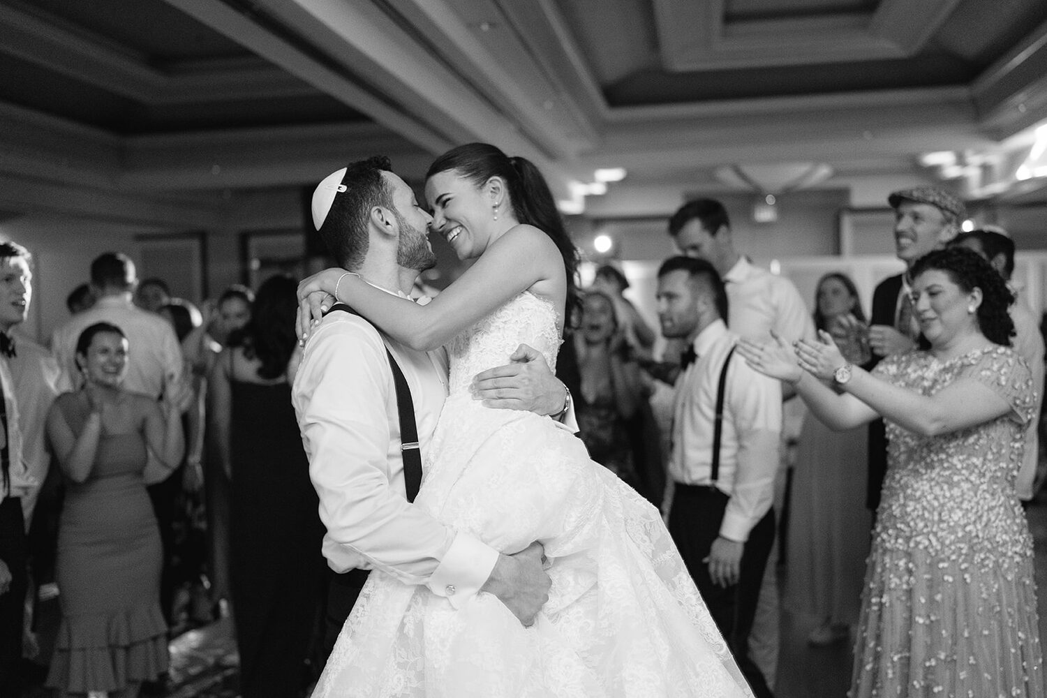 A black and white dip kiss on the dance floor, surrounded by cheering guests.