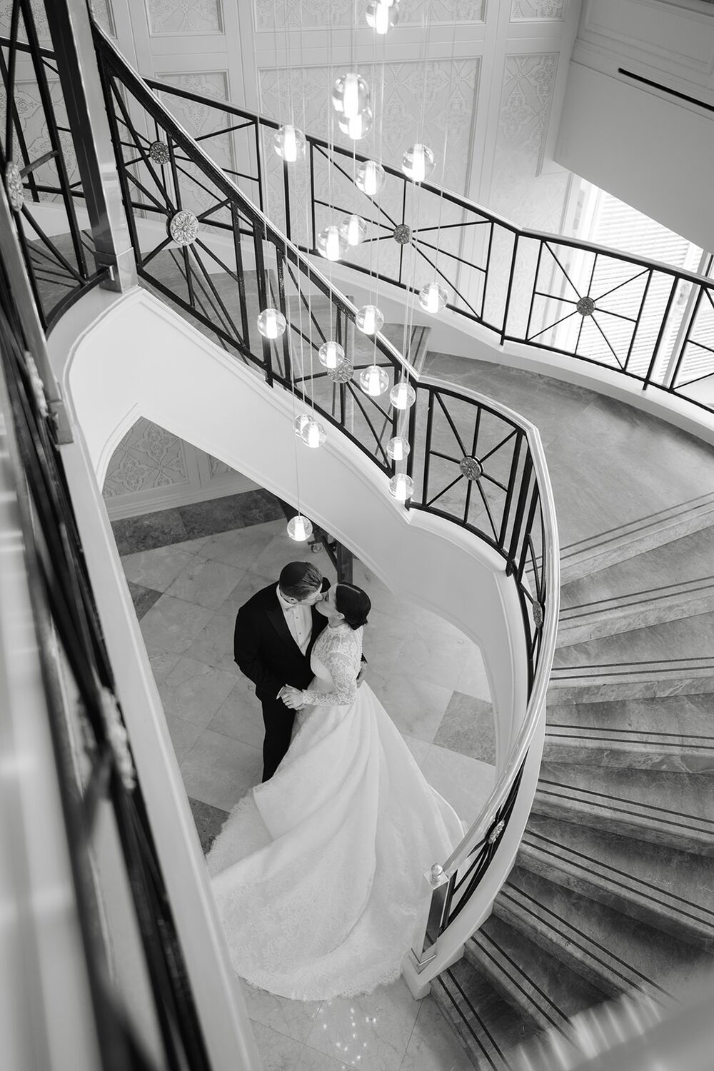 Seen from above in black and white, the couple embraces on the sweeping spiral staircase.